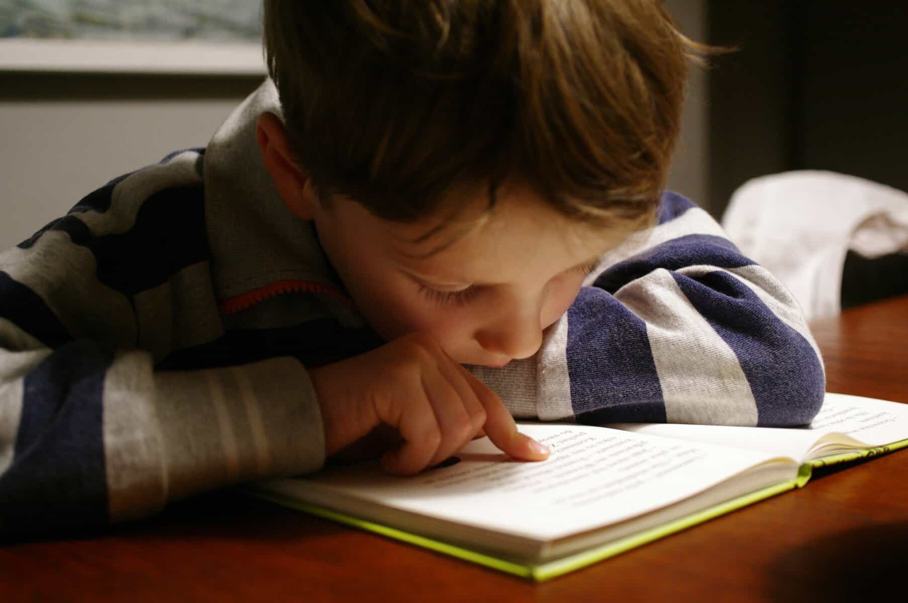 Boy leaning over an open book, tracking the words with his finger