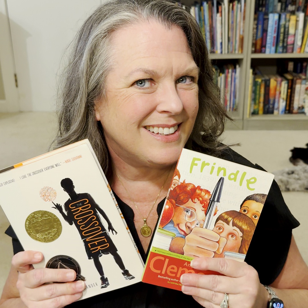 Kim Baust smiling and holding The Crossover and Frindle